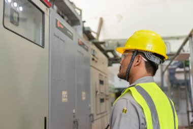 Kazan dairesinde çalışan gözlüklü Asyalı mühendis ısıtma sistemi ekipmanlarının teknik verilerini kontrol ediyor.