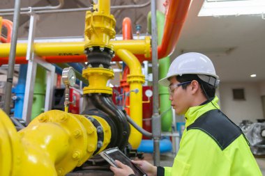 Kazan dairesinde çalışan gözlüklü Asyalı mühendis ısıtma sistemi ekipmanlarının teknik verilerini kontrol ediyor.