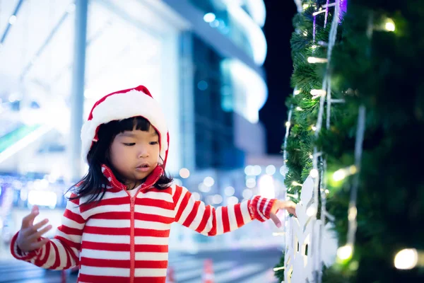 在圣诞树旁快乐地戴着圣诞帽的可爱的亚洲小女孩的画像 — 图库照片