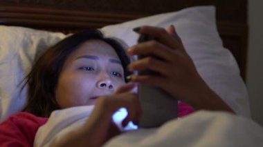 Asyalı kadın gece yatakta akıllı telefon çalar.