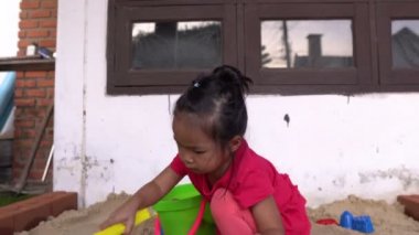 Küçük kız ön tarafta kum oynuyor, dinlenme zamanı.