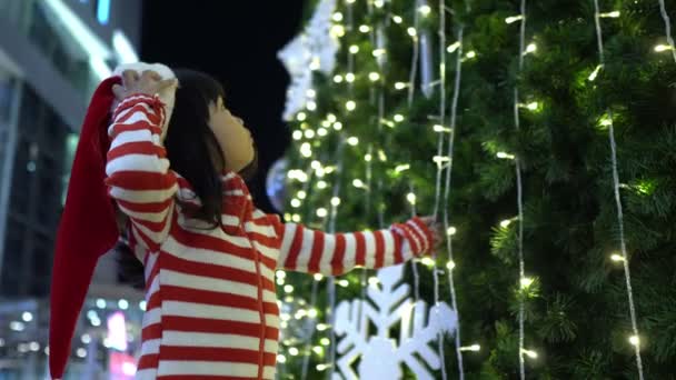 照片中可爱的亚洲小女孩头戴圣诞帽 在圣诞树旁摆姿势 — 图库视频影像
