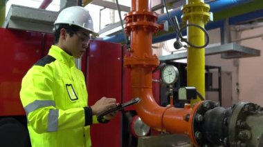 Kazan dairesinde çalışan gözlüklü Asyalı mühendis ısıtma sistemi ekipmanlarının teknik verilerini kontrol ediyor.