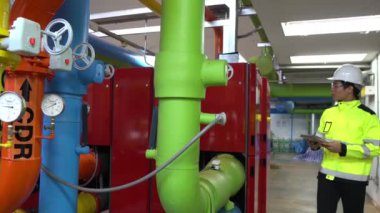 Kazan dairesinde çalışan gözlüklü Asyalı mühendis ısıtma sistemi ekipmanlarının teknik verilerini kontrol ediyor.