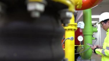 Kazan dairesinde çalışan gözlüklü Asyalı mühendis ısıtma sistemi ekipmanlarının teknik verilerini kontrol ediyor.