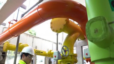 Kazan dairesinde çalışan gözlüklü Asyalı mühendis ısıtma sistemi ekipmanlarının teknik verilerini kontrol ediyor.