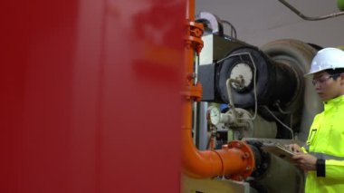 Kazan dairesinde çalışan gözlüklü Asyalı mühendis ısıtma sistemi ekipmanlarının teknik verilerini kontrol ediyor.