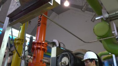 Kazan dairesinde çalışan gözlüklü Asyalı mühendis ısıtma sistemi ekipmanlarının teknik verilerini kontrol ediyor.