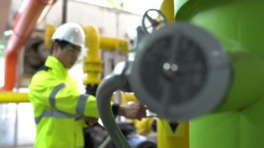 Kazan dairesinde çalışan gözlüklü Asyalı mühendis ısıtma sistemi ekipmanlarının teknik verilerini kontrol ediyor.