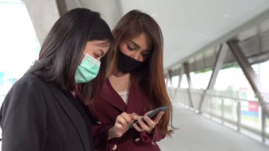 Tayland 'daki Asyalı iş kadınları koruma maskesi takıyor ve akıllı telefon kullanıyor. 
