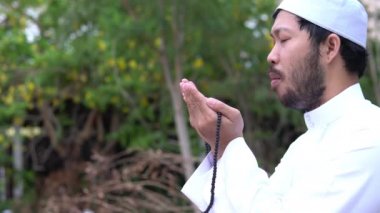 Genç Asyalı Müslüman adam gündüz vakti dışarıda namaz kılıyor, Ramazan festivali konsepti.