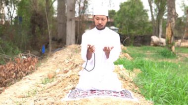 Genç Asyalı Müslüman adam gündüz vakti dışarıda namaz kılıyor, Ramazan festivali konsepti.