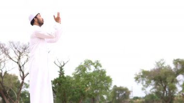 Genç Asyalı Müslüman adam gündüz vakti dışarıda namaz kılıyor, Ramazan festivali konsepti.