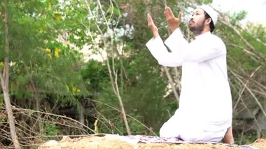 Genç Asyalı Müslüman adam gündüz vakti dışarıda namaz kılıyor, Ramazan festivali konsepti.