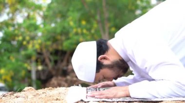 Genç Asyalı Müslüman adam gündüz vakti dışarıda namaz kılıyor, Ramazan festivali konsepti.