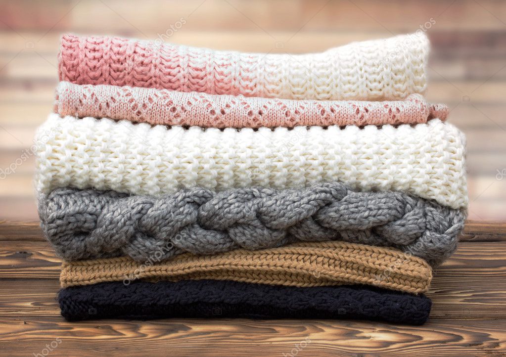 Winter knitted clothes stack on wooden background.