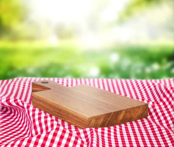 Tablero vacío de madera sobre un paño de picnic en una hierba . —  Fotos de Stock