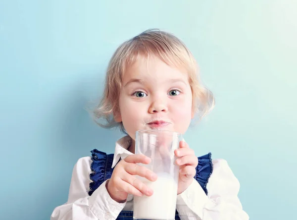 Barn flicka med glas mjölk på blå bakgrund.Kaukasiska unge p — Stockfoto