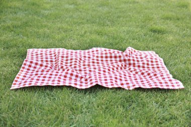Yeşil çimen arka planında kırmızı piknik battaniyesi, boş uzay gingham masa örtüsü açık hava yemek reklamları. Paskalya dekoratif arka planı..