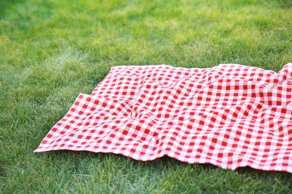Red picnic cloth towel on green grass,gingham tablecloth outdoors plaid on the ground empty copy space.Checkered towel food advertisement design.