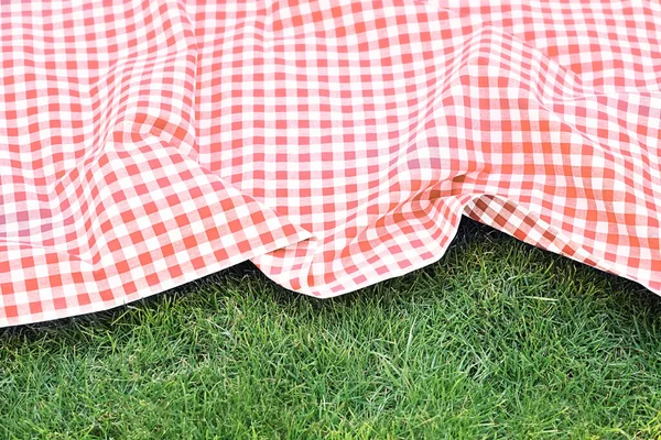 Red picnic cloth checkered tablecloth top view on green grass background,empty space food advertisement design backdrop.Gingham towel.