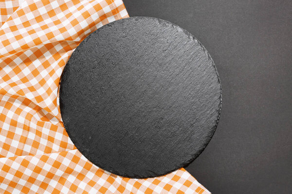 Slate black round dish empty space on dark background decorated with checkered cloth.Tableware,sushi plate.Top view backdrop.