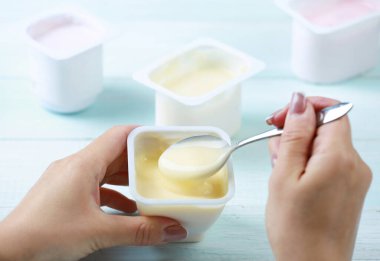 Ellerinde yoğurt paketi, yoğurt yiyen insan. Hafif yemek, abur cubur. Diyet. Kremalı tatlı..