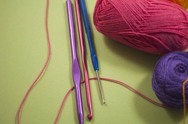 iki farklı renk ipliği ve üç pembe, mavi ve mor kanca yeşil arka planda yakın plan