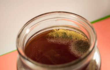 Ahududu kompostosu ile kapağı olmayan yarım kavanoz, tamamen sarı ve gri küf iplikleriyle kaplı. Fotoğraf beyaz-pembe arka planda. Mikroorganizma kolonileri.