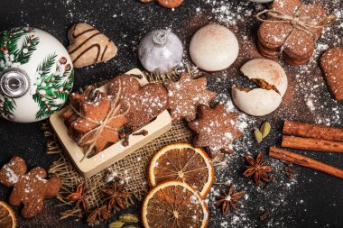 Siyah arka planda pudra şekerli zencefilli kurabiye. Pekmezden yapılmış ve zencefilli kurabiyeler. Beyaz Noel ağacı süslemeleri olan bir Noel kompozisyonu. Yıldız anason, tarçın çubukları, portakal dilimleri ve diğer baharatlar. Yeni yıl havası.