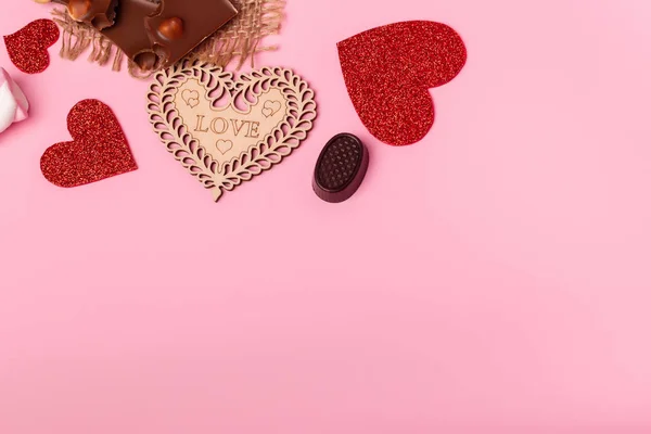 Valentine\'s day atmosphere and romantic mood. Milk chocolate with nuts/ dark chocolate candies and red hearts on a pink background.