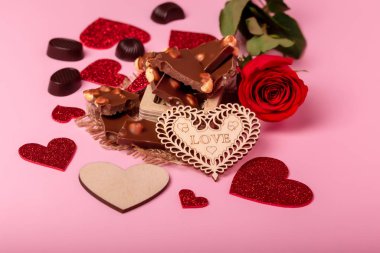 Valentine's day background with red hearts, chocolate candies, milk chocolate and red rose on a pink background. Romantic atmosphere and love symbols.