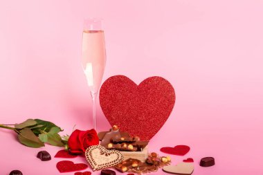 Sevgililer günü atmosferinde kırmızı kalpler, çikolata şekerler ve pembe arka planda şampanya kadehleri. Gül ve kırmızı kalpler. Romantik bir ruh hali. Aşk atmosferi.