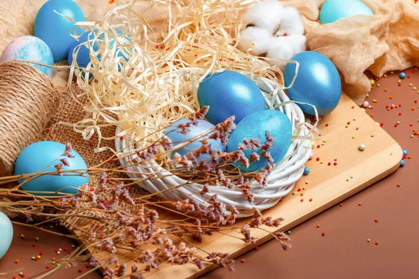 Easter composition with dyed eggs in the nest on a brown background. Blue Easter eggs. Colored eggs in the nest. Rustic composition with easter atmosphere.