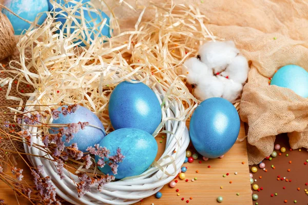 Easter composition with dyed eggs in the nest on a brown background. Blue Easter eggs. Colored eggs in the nest. Rustic composition with easter atmosphere.