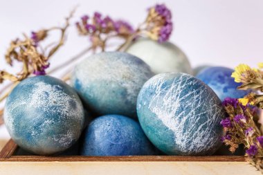 Ahşap bir kutuda boyanmış paskalya yumurtaları ve beyaz arka planda bahar çiçekleri.. 