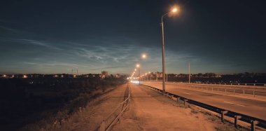 Gece şehir yolu alacakaranlıkta sokak lambalarıyla aydınlatılmış gümüşi bulutların arka planına karşı. Karanlık tasarımlar ve iç mekanlar için harika.