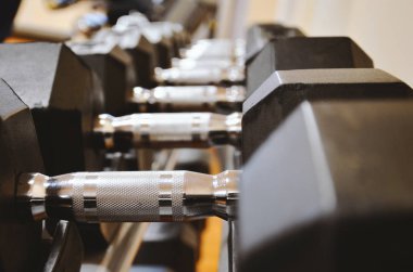 Spor salonunun arka planında bulanık bir arka plan ile odak noktasında duran farklı ağırlıklardan oluşan siyah kauçuk halterler.