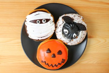 Üç farklı Cadılar Bayramı Donutu 'nun Tahta Masa' da servis edilen siyah tabakta üst görünümü
