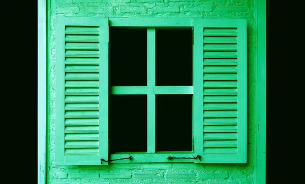 Lime green colored wooden window with shutters on green brick wall