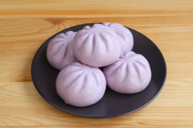 Heap of purple sweet potato steamed buns on black plate served on wooden table