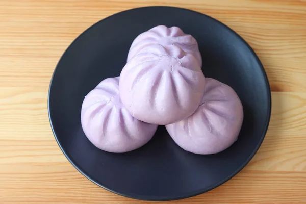Plate of purple sweet potato steamed buns served on wooden table