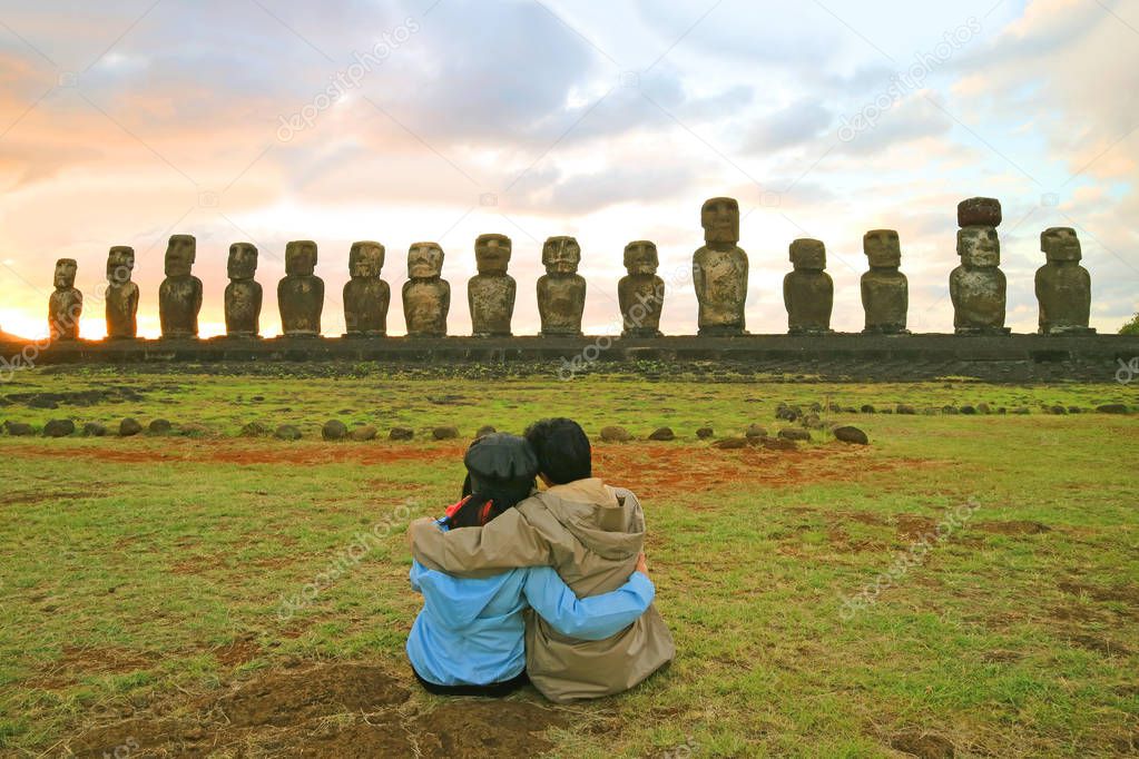 Couple having a happy moment in front of the awesome Moai statues of Ahu Tongariki at sunrise, Easter Island, Chile