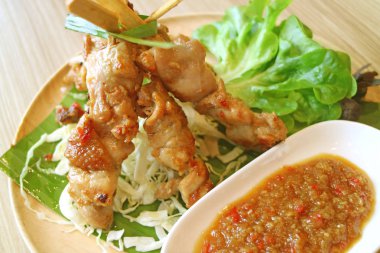 Baharatlı sos ve ahşap tabakta servis edilen yeşil salatalı ızgara tavuk.