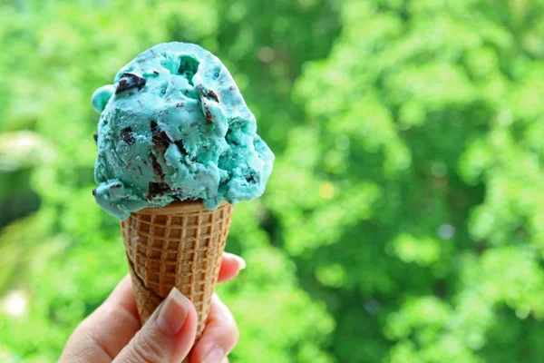 Рука Держит Мятное Мороженое Шоколадной Крошкой Конусе Против Размытой Зеленой — стоковое фото