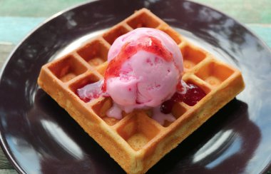Koyu kahverengi tabakta çilekli kremayla kaplanmış taze pişmiş waffle.