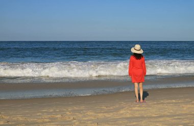 Sahildeki su sıçratan dalgaya bakan kadın.