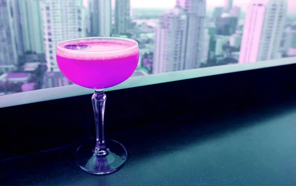 Shocking pink colored cocktail on the rooftop bar's table with skyscrapers view in the backdrop