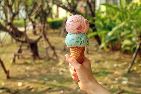 Two scoops of ice cream cone in woman\'s hand with blurry sunshine garden in background