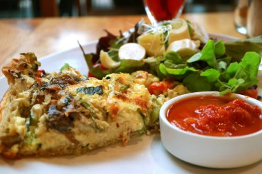 Yeşil salata ve kırmızı baharatlı soslu Kiş Lorraine tabağı.